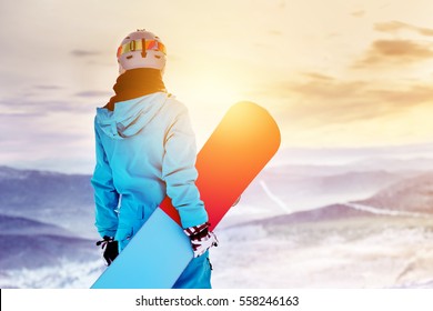 Girl snowboarder stands with snowboard on mountain's top on sunrise backdrop. Sheregesh ski resort - Powered by Shutterstock