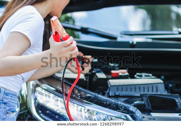 The girl is solving the problem. The car rental is\
not started after driving to travel in the forest.\
The girl is\
carrying a Jumper line to stimulate the car battery while waiting\
for the service team