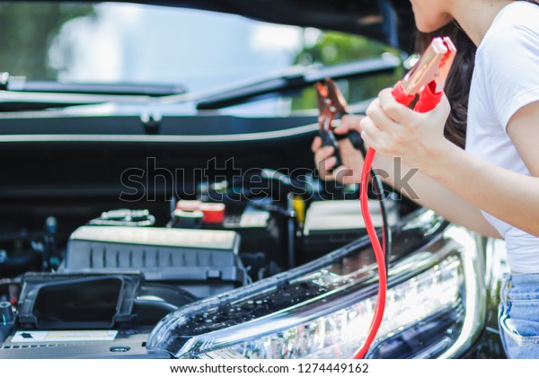 The girl is solving the problem. The car rental is\
not started after driving to travel in the forest.\
The girl is\
carrying a Jumper line to stimulate the car battery while waiting\
for the service team