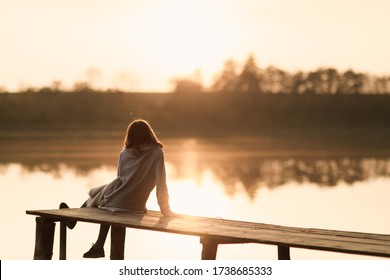 The girl spends time by the water in the woods. Dressed in a cardigan. Have fun and watch the sunset. Silhouette.