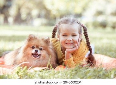 A girl and a Spitz dog, a child lies in the park on the grass, next to a girl a fluffy Spitz dog, a baby smiles, a portrait of a child and an animal. Taking care of pets.