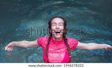 Girl in splashes of water with her mouth open and her eyes closed stands in a turquoise river