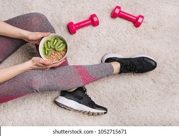 girl in sporting elk holds a plate with muesli and kiwi after fitness workout with dumbbells