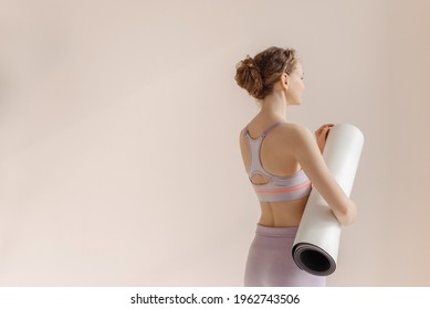 Girl with a sports mat is preparing for workout. Young woman on a beige one ton background. - Powered by Shutterstock