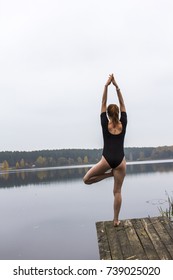 Girl with a sports sexy figure is engaged in sports yoga stretching fitness on background of a calm autumn river lake.