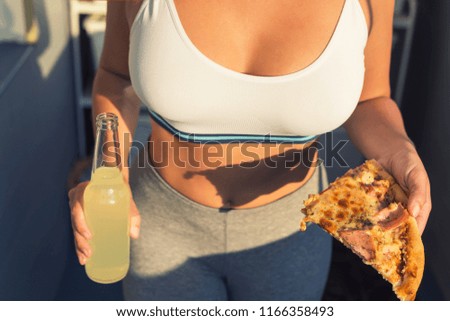 	
A girl in a sports suit holds a huge piece of pizza. Concept