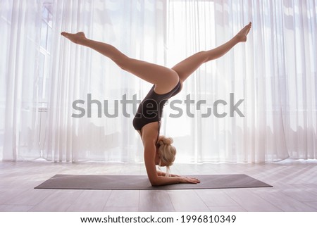 A girl in a sports swimsuit does yoga - does a handstand on the mat