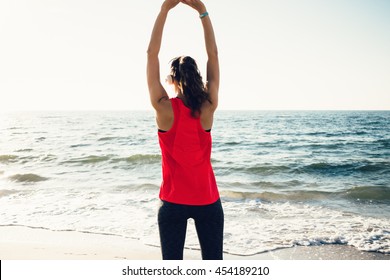 Girl in sportswear doing morning exercises on the beach and listening to music on headphones, view from the back - Powered by Shutterstock