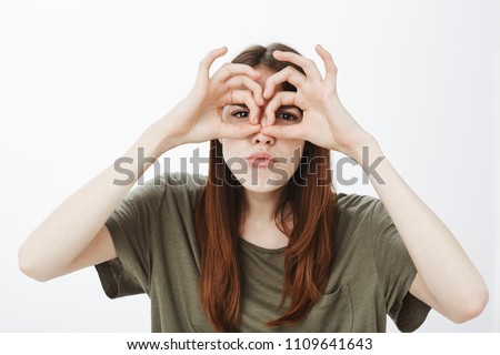 Girl spying on friend with fake goggles. Portrait of good-looking female student with funny expression, holding okay gestures over eyes, mimicking binocular, making serious childish face