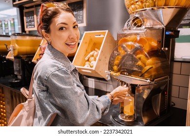 A girl squeezes fresh orange juice in a juicer in a supermarket - Powered by Shutterstock