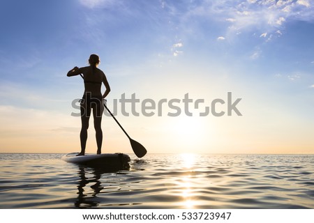 Girl stand up paddle boarding (sup) on quiet sea at sunset