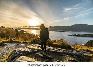girl standing with backpack with her back against the sun with halo at the Aksla observation deck overlooking the mountains during sunrise