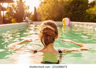 Girl standing backwards in the outdoor swimming pool. Garden in the background. Summer holiday (vacation) fun and recreation.