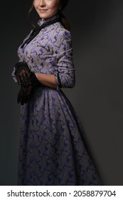 A girl standing in a blue dress in the style of the 1900s, in a retro dress, a hat on a gray background. Historical fashion of the 19th century. High quality photo