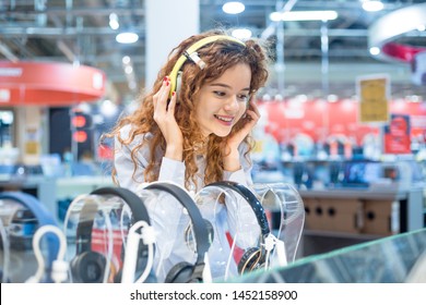  Girl Standing In Front Of The Stand In The Electronics Store Chooses Headphones Before Buying Wearing On Her Head Listening To The Sound