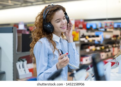  Girl Standing In Front Of The Stand In The Electronics Store Listening To Music In Headphones