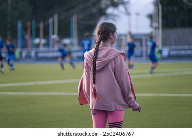 girl standing and looking at football players, blue football players uniform, football field, game, childhood, child, baby, kid - Powered by Shutterstock