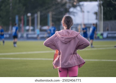 girl standing and looking at football players, blue football players uniform, football field, game, childhood, child, baby, kid - Powered by Shutterstock