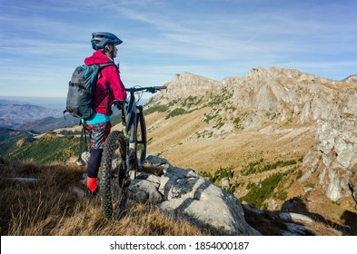 Girl standing next to her mountain bike on top of a cliff and admiring Bucegi mountains in Romania