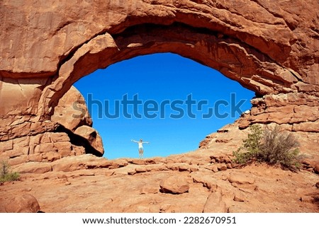 Girl standing in North Window Arch, a stone arch of red sandstone formed by erosion, Arches-Nationalpark, near Moab, Utah, United States