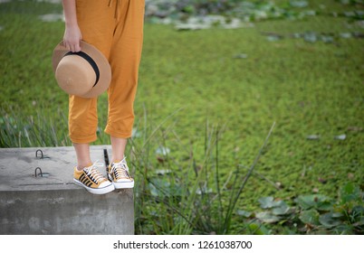 Girl is standing on the concreate with yellow sneaker and holding brown hat.