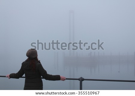 A girl standing on the edge of Lake Constance (Bodensee) in foggy weather in Bregenz, Vorarlberg, Austria.