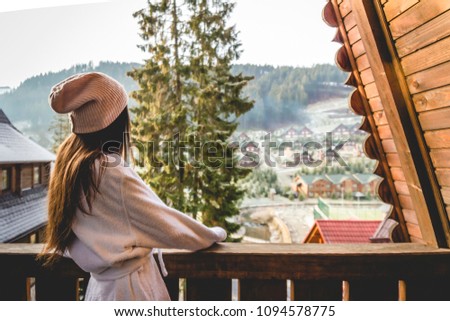 The girl is standing on a terraced house in a mountainous area. In good winter weather.