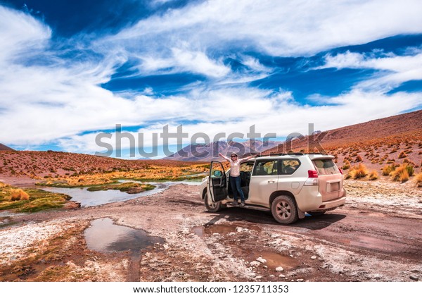 Girl standing\
at the opened car door with raised hands and taking pleasure of\
exciting landscape of\
Bolivia