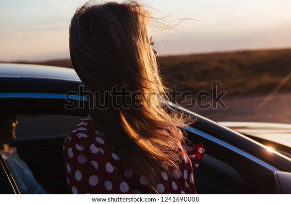 A girl stands by the\
car on the road