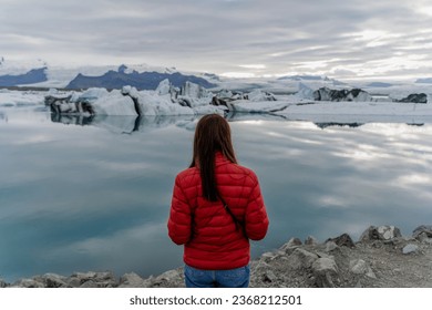The girl stands with her back against the background of a melting glacier. Iceland.