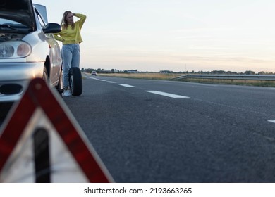 girl in stands near the rear wheel of the car and rolls a spare wheel to change it.A car breakdown, the wheel in front is a temporary stop sign blurred on the right there is a place for an - Shutterstock ID 2193663265