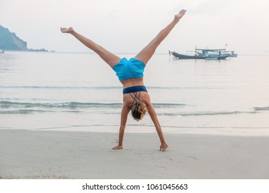 a girl stands on her hands on a sandy beach, enjoys life with freedom and youth - Powered by Shutterstock