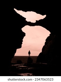 Girl stands on a rock in a famous Yoda cave (Gígjagjá) with beautiful pink sky with clouds. Iceland hidden gems - Hjörleifshöfði mountains	