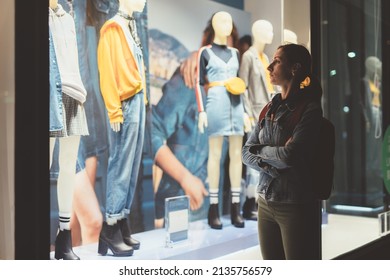 Girl Stands Outside The Store And Looks At The Female Clothes On The Mannequins.