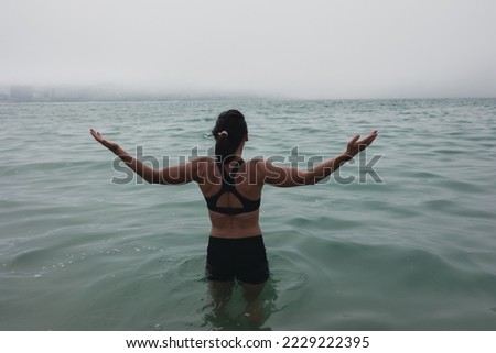 The girl stands in the water of the ocean, hands to the sides. He looks into the fog in the distance.