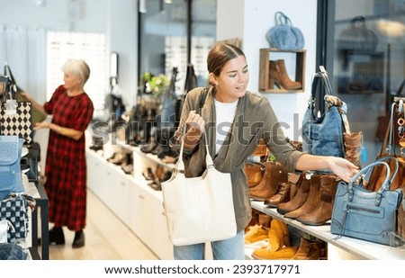 Girl in store eye windowshopping product she likes and tactilely checks authenticity and naturalness of leather material from which bag is made. Buyer examines quality of material and execution