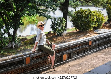 girl in a straw hat sits on a fence and looks into the depths of the park