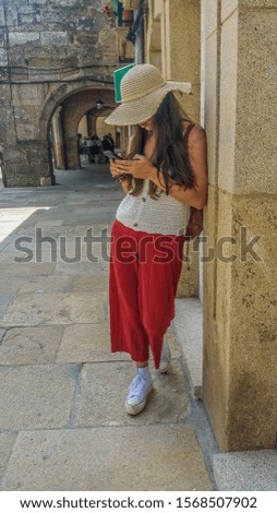 girl in a street with a hat and red trousers using the mobile phone
