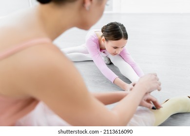 Girl Stretching On Floor In Ballet School Near Blurred Dance Teacher