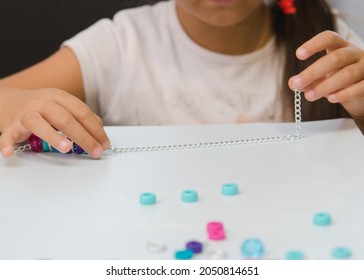 The girl is stringing blue and pink beads from the creativity kit on a chain. Fine motor skills, development of children. Close-up. Blur, concept