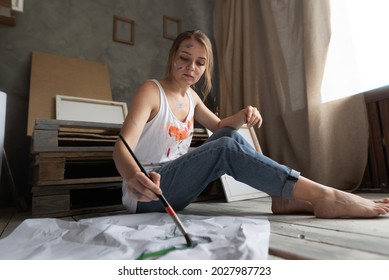 a girl student artist sits the floor in an art studio holding brush in her hands   draws crumpled piece paper 
