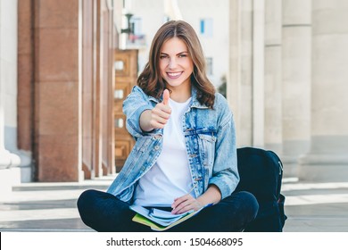 Girl student sitting near the university and shows like gesture. The girl passed the exam perfectly