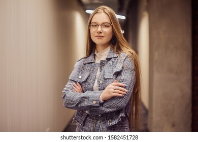 Girl Student Stands In The Corridor Of The University / University Dormitory. The Blonde Is Looking At The Camera. A Student With Glasses Stit In The Hallway.