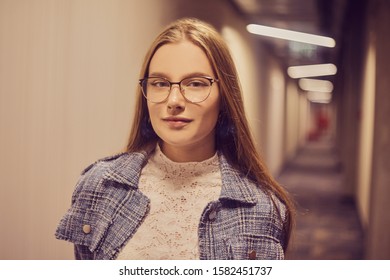 Girl Student Stands In The Corridor Of The University / University Dormitory. The Blonde Is Looking At The Camera. A Student With Glasses Stit In The Hallway.