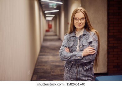 Girl Student Stands In The Corridor Of The University / University Dormitory. The Blonde Is Looking At The Camera. A Student With Glasses Stit In The Hallway.