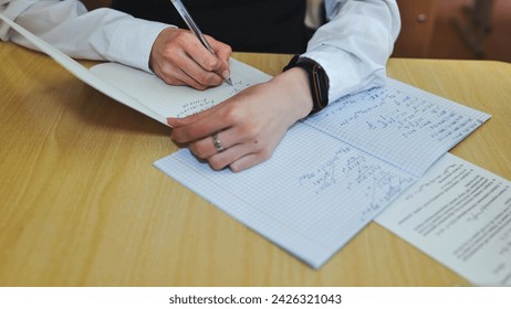 A girl student writes math formulas in a notebook. Notebook close-up.