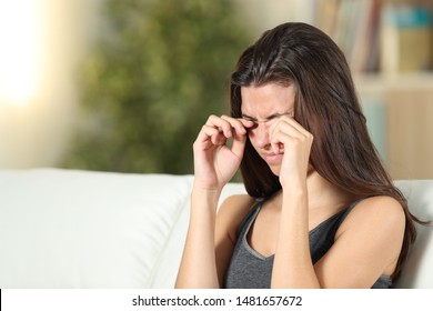 Girl suffering itching scratching eyes sitting on a couch in the living room at home