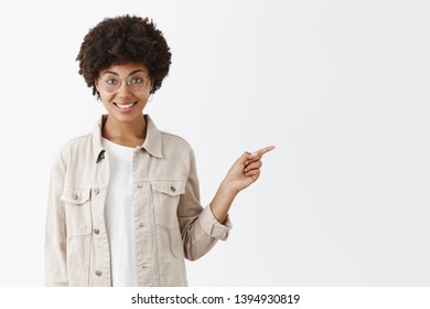 Girl Suggesting Grab Some Coffee And Continue Conversation In Lovely Cafe. Portrait Of Charming African American In Glasses And Shirt With Afro Hairstyle, Pointing Right With Index Finger And Smiling