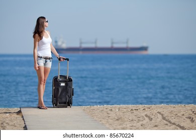 Girl With Suitcase On The Beach. Attractive Young Woman With Rolling Suitcase On The Beach.