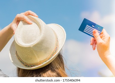 Girl In A Summer Hat Holds A European Health Insurance Card Against The Sky.  Concept, Travel Insurance, Holiday Security, Treatment Abroad